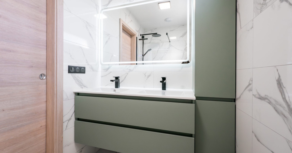 Aménagement d'une salle de bain moderne à Mulhouse avec meuble double vasque vert sauge, miroir rétroéclairé LED et carrelage effet marbre.